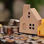 Cozy miniature house models surrounded by scattered coins, representing real estate investment, property management, and housing market themes in a financial or residential context.