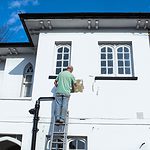 man in yellow shirt and blue denim jeans standing on white concrete building during daytime